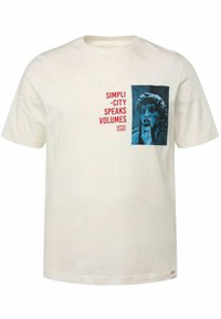 Krémové tričko vyrobené z bavlny, s modrou grafikou obličeje a červeným textem, který říká "JEDNODUCHOST MLUVÍ HLASITĚ." Krátké rukávy.