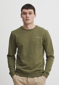 O sweatshirt verde oliv cu guler rotund, manșete ribbed și un mic logo "CASUAL" pe piept. Material moale, texturat.