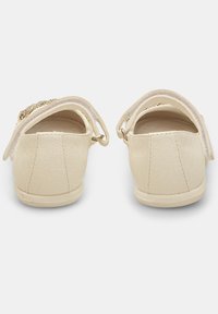 Weiße Kinder Schuhe aus Kunstleder mit flacher Sohle, elastischen Riemen und dekorativem Zubehör vorne. Glatte Textur und runde Form.