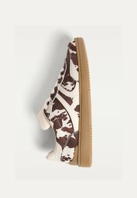 Brune og hvide sneakers med cow-print, der har en beige lædertunge, beige detaljer og en gummisål. Har runde snørebånd og teksturerede materialer.