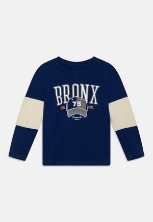 Camicia a maniche lunghe blu navy con accenti crema, presenta la grafica "BRONX 75" in bianco e grigio. Materiale in cotone morbido, stile colletto rotondo.