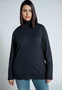 Dunkelgrauer Rollkragenpullover mit langen Ärmeln, mit einem strukturierten Saum und lockerer Passform. Kombiniert mit hellblauen Jeans.