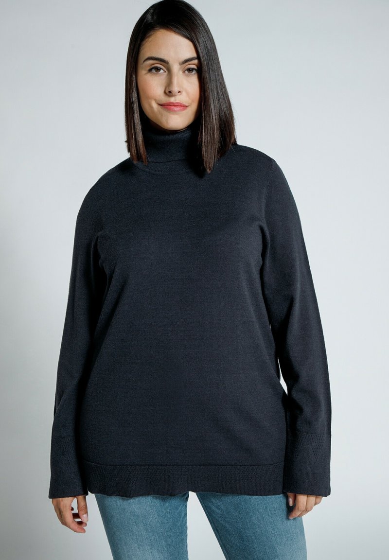 Dunkelgrauer Rollkragenpullover mit langen Ärmeln, mit einem strukturierten Saum und lockerer Passform. Kombiniert mit hellblauen Jeans.