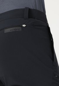 Svarta utomhusbyxor med en stilren design, texturerad tyg, diskret logotyp på midjebandet och en ficka med dragkedja för förvaring.