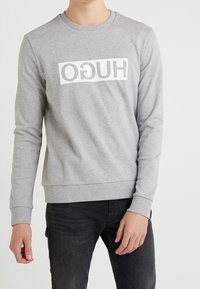 Grauer Langarm-Sweatshirt aus Baumwolle mit zentralem weißen "HUGO"-Logo, rundem Ausschnitt und gerippten Bündchen sowie Saum.