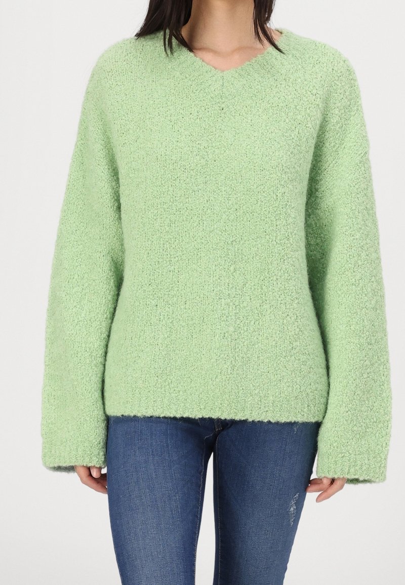 Pull en maille vert clair, surdimensionné, avec col en V et manches larges. Tissu doux et texturé avec un ourlet légèrement raccourci.