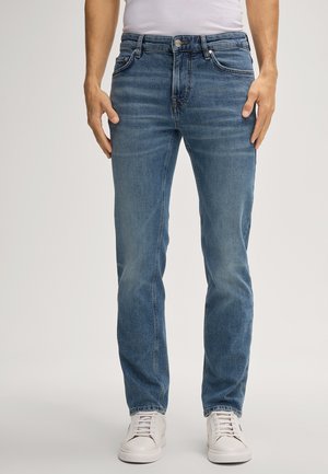 Dark blue denim jeans with a slim fit, five-pocket design, contrast stitching, and a faded finish. Worn with white sneakers.