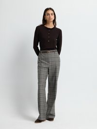 Maglietta marrone a maniche lunghe con scollatura arricciata e dettagli di bottoni, abbinata a pantaloni grigi a quadri con gamba dritta e cintura.