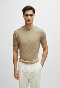 T-shirt beige a girocollo con maniche corte, realizzata in morbido tessuto di cotone. Abbinata a pantaloni a quadri chiari e una cintura marrone chiaro.