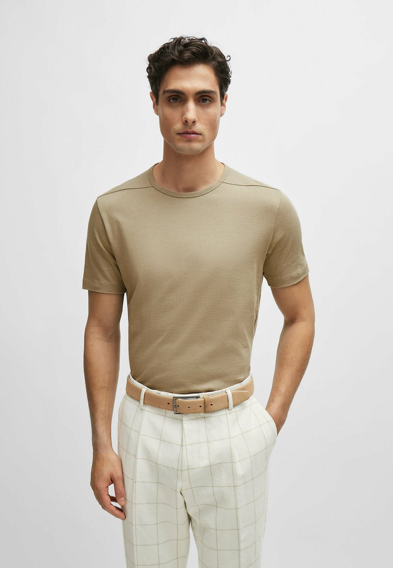 T-shirt beige a girocollo con maniche corte, realizzata in morbido tessuto di cotone. Abbinata a pantaloni a quadri chiari e una cintura marrone chiaro.