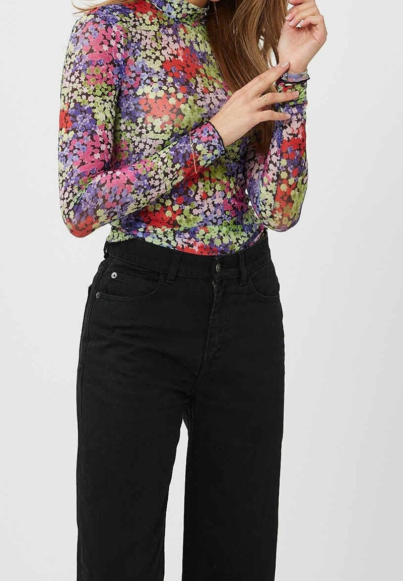 Långärmad, genomskinlig polotröja med ett färgglatt blommönster, i nyanser av rosa, lila, röd och grön, kombinerad med svarta byxor.