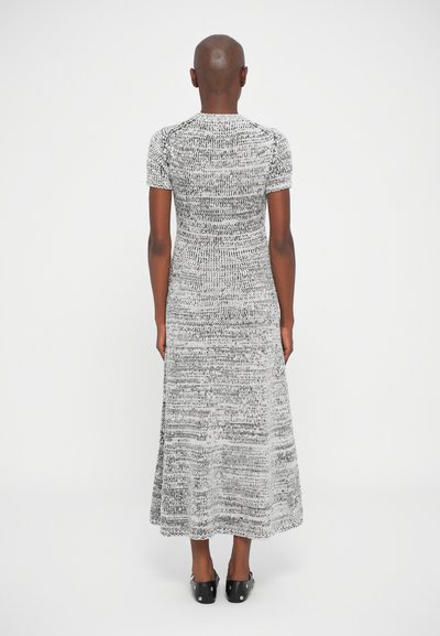 Persona vista di spalle che indossa un vestito corto a maniche corte a maglia bicolore nero e bianco con una gonna svasata e scarpe slip-on nere con borchie.