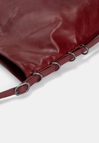 Rote Leder-Tote-Tasche mit glatter Oberfläche, ausgestattet mit silbernem Beschlag und großen runden Ringen entlang der Kante. Verstellbarer Schulterriemen enthalten.