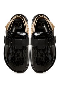 Zapatos de charol negros con acabado texturizado, correa negra ajustable y una banda decorativa beige contrastante en el tacón.