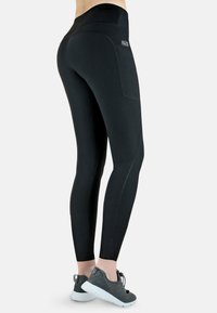 Schwarze Leggings aus elastischem Stoff mit hohem Bund, ausgestattet mit einer Seitentasche und kontrastierenden Nähdetails.