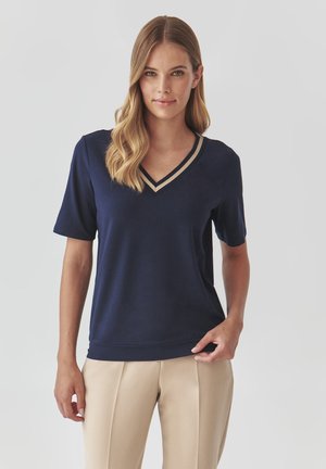 Marineblå kortærmet top med V-hals og kontrasterende beige kant. Blødt materiale med en afslappet pasform, som er parret med beige bukser.