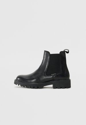 Bottes Chelsea en cuir noir avec des panneaux élastiques sur les côtés, une languette de tirage et une semelle en caoutchouc épaisse et texturée. Fini lisse avec un design durable.