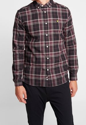 Mand iført en knappet, langærmet skjorte i sort og mørkerød tern med en lille gul fuglelogo på brystet, kombineret med sorte bukser.