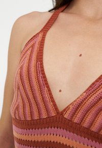 Gros plan d'une personne portant un top au col halter en tricot avec des rayures verticales dans des tons d'orange, de rose et de marron.