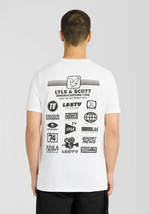 Mann trägt ein weißes Lyle & Scott T-Shirt mit verschiedenen schwarzen Medien- und Rundfunklogos auf dem Rücken.
