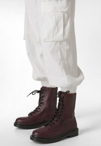 Bordeauxkleurige veterschoenen in militaire stijl met een rits aan de zijkant, stevige zwarte rubberen zolen, gecombineerd met witte cargobroeken met elastische boorden en zakken.