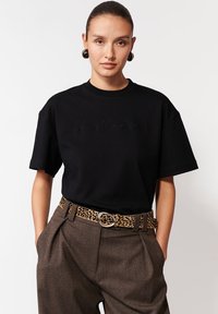 Czarny t-shirt z krótkim rękawem z haftowanym logo "La Maria", zestawiony z brązowymi spodniami o wysokim stanie i paskiem w cętki.