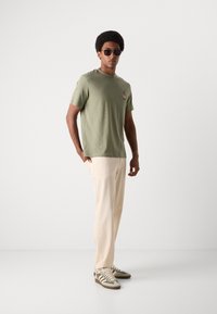 Groene katoenen t-shirt met een klein ontwerp, beige relaxed-fit broek en grijs-gestreepte sneakers accentueren de casual outfit. Zonnebril inbegrepen.