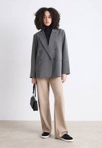 Blazer doppiopetto grigio a righe sottili, dolcevita nero, pantaloni beige a gamba larga, sneaker nere e piccola borsa nera.