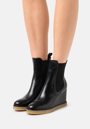 Bottines en cuir noir avec des panneaux élastiques sur les côtés, des talons en coin effilés et une semelle en caoutchouc texturée. Design classique avec un minimum de détails.