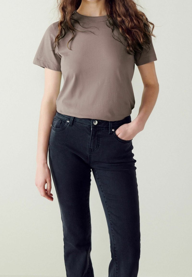 T-shirt marron à manches courtes en coton, associé à un jean noir ajusté avec une fermeture à bouton et des poches latérales.