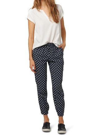 Tmavě modré vzorované kalhoty se stahovací šňůrkou v pase a zúženými kotníky, doplněné krátkým bílým tričkem. Obuv tvoří tmavé nazouvací boty.