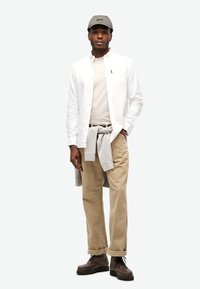 Camisa blanca de botones, camiseta beige, pantalones de pana beige, suéter gris atado a la cintura, gorra gris, botas marrones con cordones. Diseño minimalista.