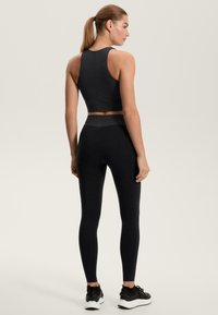 Čierny športový komplet so štruktúrovaným krátkym topom s vysokým golierom a zodpovedajúcimi legínami s vysokým pásom, oba z pružnej látky.