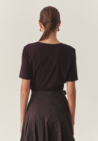 Bordowa koszulka z krótkim rękawem z okrągłym dekoltem, zestawiona z czarną spódnicą o wysokim stanie z fałdami wykonaną z gładkiego materiału.