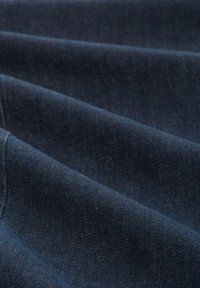 Tissu en denim bleu foncé avec une texture douce, présentant un léger brillant. Le matériau est plié, mettant en valeur son poids et sa profondeur.