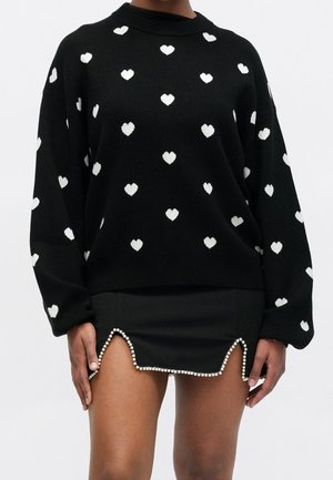 Sort sweater med hvide hjerteprints kombineret med en sort mininederdel med bølget kant, der er pyntet med perler.