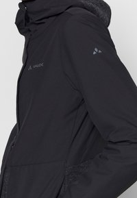 Svart vindjacka med huva, mjukt texturerat tyg vid kragen och subtil logotyp på bröstet och ärmen.