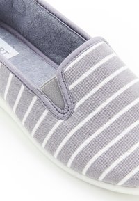 Scarpa slip-on grigia con strisce orizzontali bianche, tomaia in tessuto, pannelli laterali in elastan, interno imbottito e suola in gomma bianca.