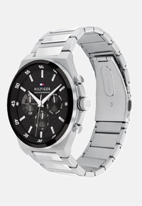 Montre en acier inoxydable argenté avec un cadran noir texturé, des marqueurs d'heure blancs et des fonctions de date. Elle est dotée d'une lunette noire et de deux boutons poussoirs.