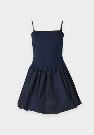 Mornarsko plava haljina s prilagođenim gornjim dijelom i raširenom, naboranom suknjom. Izrađena od glatkog materijala s trakama poput tjestenine.