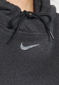 Grå huvtröja i mjukt tyg, med en svart dragsko och en glittrig silverfärgad Nike-logga på bröstet.