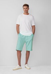 Witte korte mouwen t-shirt gecombineerd met mintgroene shorts. Schoenen zijn beige met witte veters. Eenvoudig ontwerp, relaxte pasvorm, geen zichtbare patronen.