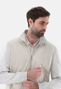 Helle beige Zip-Jacke mit kontrastierenden cremefarbenen Ärmeln, Stehkragen, strukturiertem Stoff und silbernen Hardware-Details.