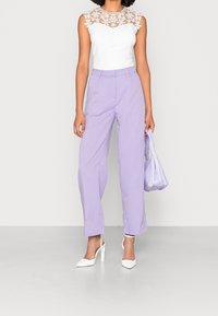 Vit ärmlös topp med spetsdetaljer och blommiga accenter, kombinerad med högmidjade lavendelfärgade byxor och vita slingback-hälar.