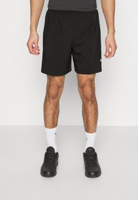 Pantalones cortos deportivos negros con una cintura elástica, tela ligera y bolsillos laterales. Se lleva con zapatillas negras y calcetines blancos.