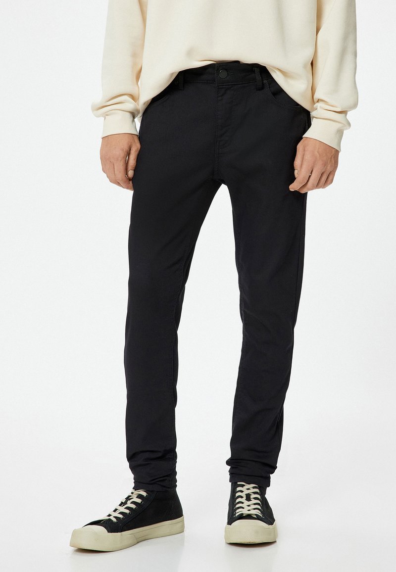Pantalones negros ajustados, hechos de un tejido ligero. Presentan bolsillos frontales y un cierre de botón, combinados con zapatillas altas negras.