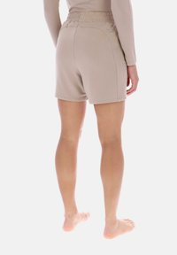 Pantalones cortos deportivos beige con cintura elástica, textura suave y dos bolsillos traseros, mostrados desde atrás.