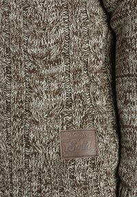 Brown knitted sweater with a textured cable pattern and a leather label featuring the word "Solid." Light and dark brown yarn mix.