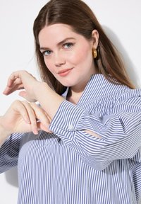 Camicia a righe blu e bianche con colletto alto e maniche arrotolate, caratterizzata da una vestibilità ampia e una texture di tessuto morbida.