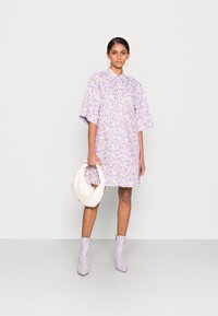 Vestido de manga curta em tecido lavanda com estampa de margaridas, combinado com uma bolsa creme e botas de tornozelo lilás. Design de gola simples.